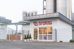 Rapsody of Spices Laden auf dem Produktionsgelände von Raps in Kulmbach, sehr kleines Gebäude vor Fabrikgelände mit Gewürzsilos im Hintergrund