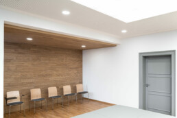 Moderner Raum, die Wand links ist mit Holz verkleidet, davor stehen Stühle