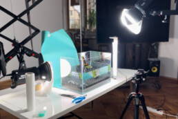 Bild aus dem Fotostudio Kingunion, eine Bierflasche steht in Aquarium, davor steht ein Kamerastativ, darum herum hängen zwei Studiolampen