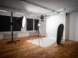 Fotostudio Kingunion, weißer Studiohintergrund ist ausgerollt, davor steht ein LED-Dauerlicht mit Lightbox und eine Flächenleuchte, eine Kamera auf Stativ, rechts ein Faltreflektor, darüber ein Deckenschienensystem